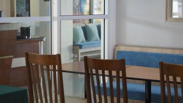 A dining area with a glass table, wooden chairs, and a blue sofa in the background.
