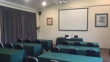 A conference room with tables and chairs, a projector screen, and a framed picture on the wall.