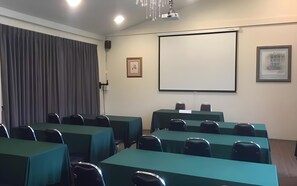 A conference room with tables and chairs, a projector screen, and a framed picture on the wall. - Phromsuk Hotel Ayutthaya (Phra Nakhon Si Ayutthaya)