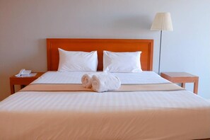 Un lit bien fait, avec des draps blancs, deux oreillers et une serviette enroulée posée sur le lit.