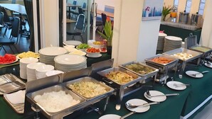 A buffet setup with various food items and stacked plates. - Phromsuk Hotel Ayutthaya (Phra Nakhon Si Ayutthaya)