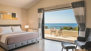 Ein Hotelzimmer mit Bett, einem Sessel, einem kleinen Tisch und Meerblick durch große Fenster.