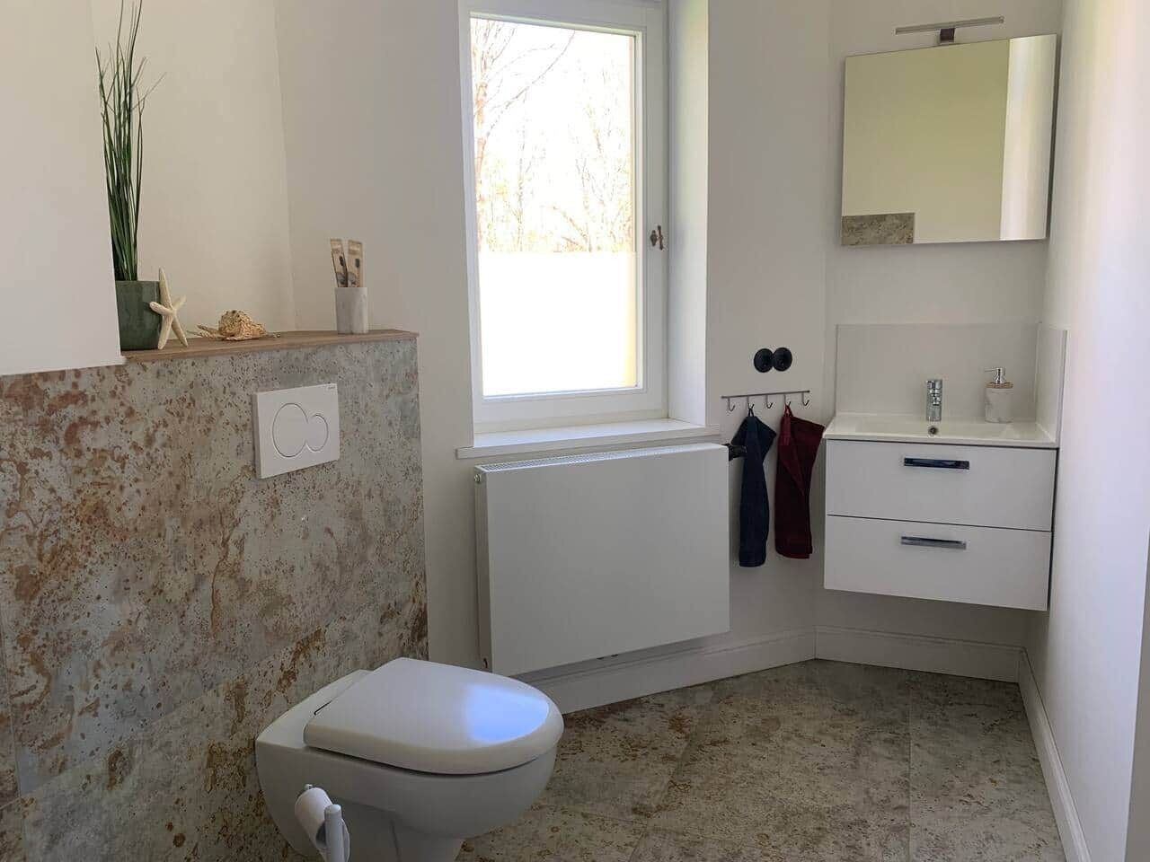 Une salle de bain comprenant des toilettes, une fenêtre, un radiateur, un miroir et un lavabo.