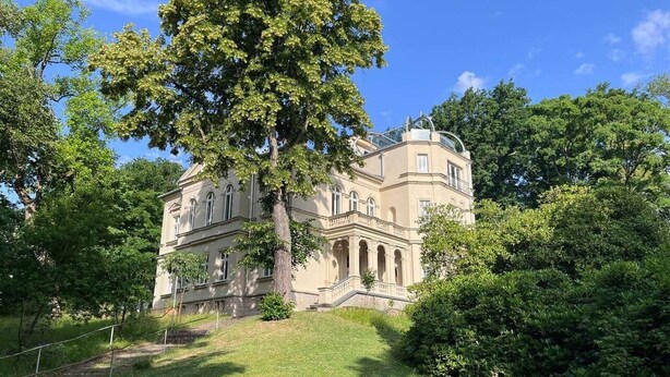 A large, historic building with a prominent entrance, surrounded by lush greenery and trees. - NEW! Vogtland Herberge Auerbach 3 persons + baby (Auerbach)