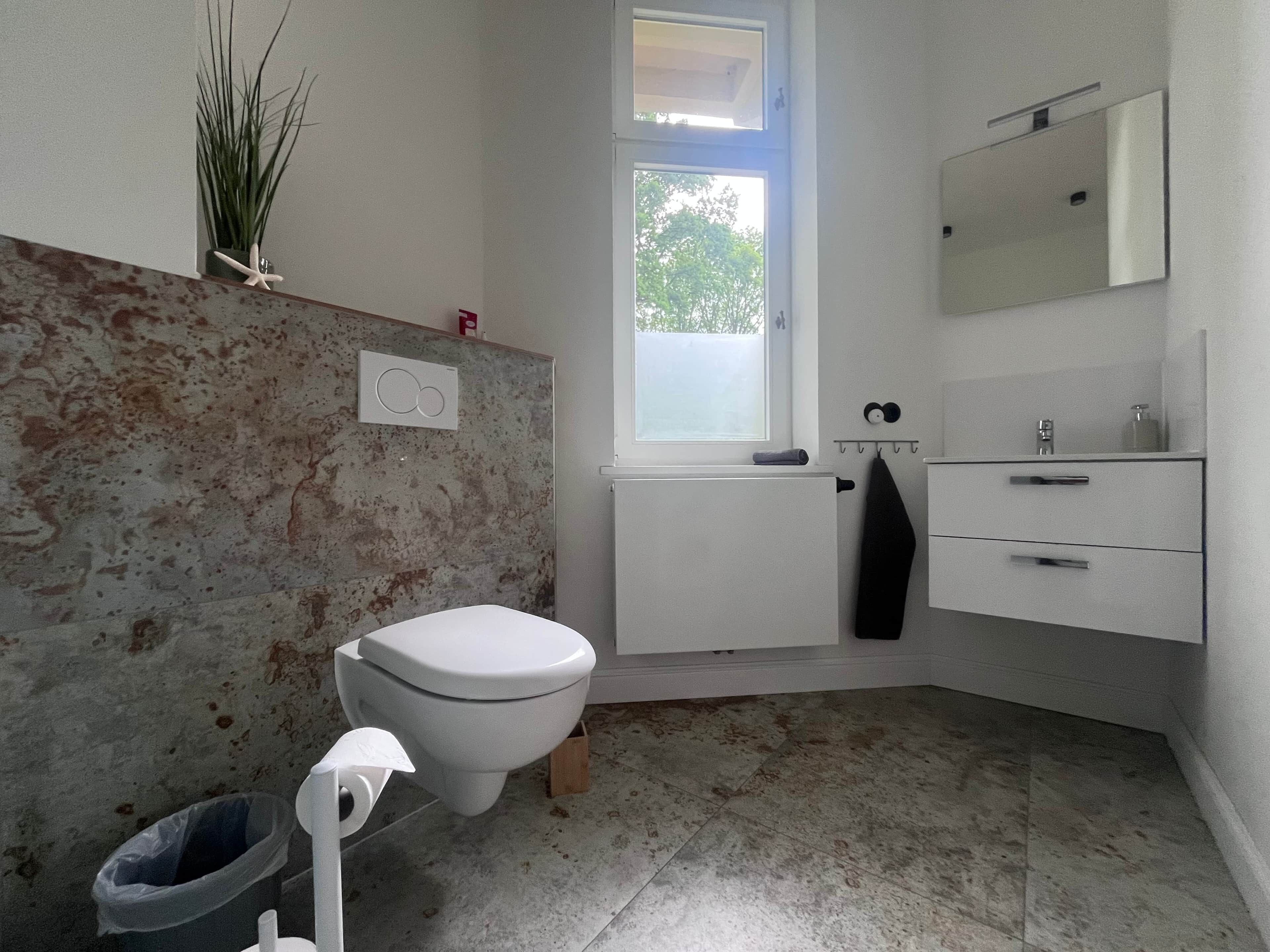 Une salle de bain avec des toilettes, un lavabo, un miroir et une fenêtre.