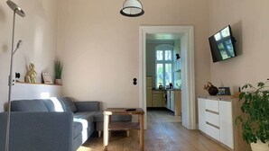 A modern living room with a sofa, a small wooden table, a floor lamp, a TV mounted on the wall, and a potted plant. - NEW! Vogtland Herberge Auerbach 3 persons + baby (Auerbach)