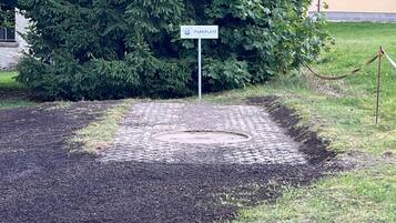 Een verhard gebied met een bord waarop 'Parkplatz' staat, omringd door groen en een gebouw met een blauw dak.