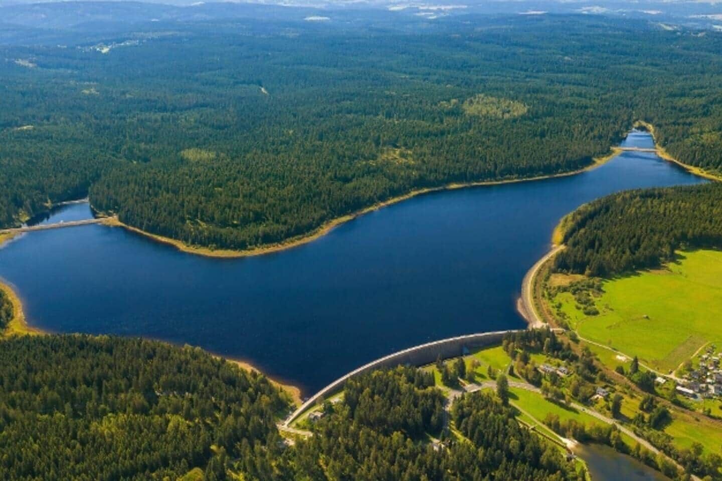 Ein weiter See, umgeben von dichten Wäldern, mit einer Brücke, die zwei Landstriche miteinander verbindet.