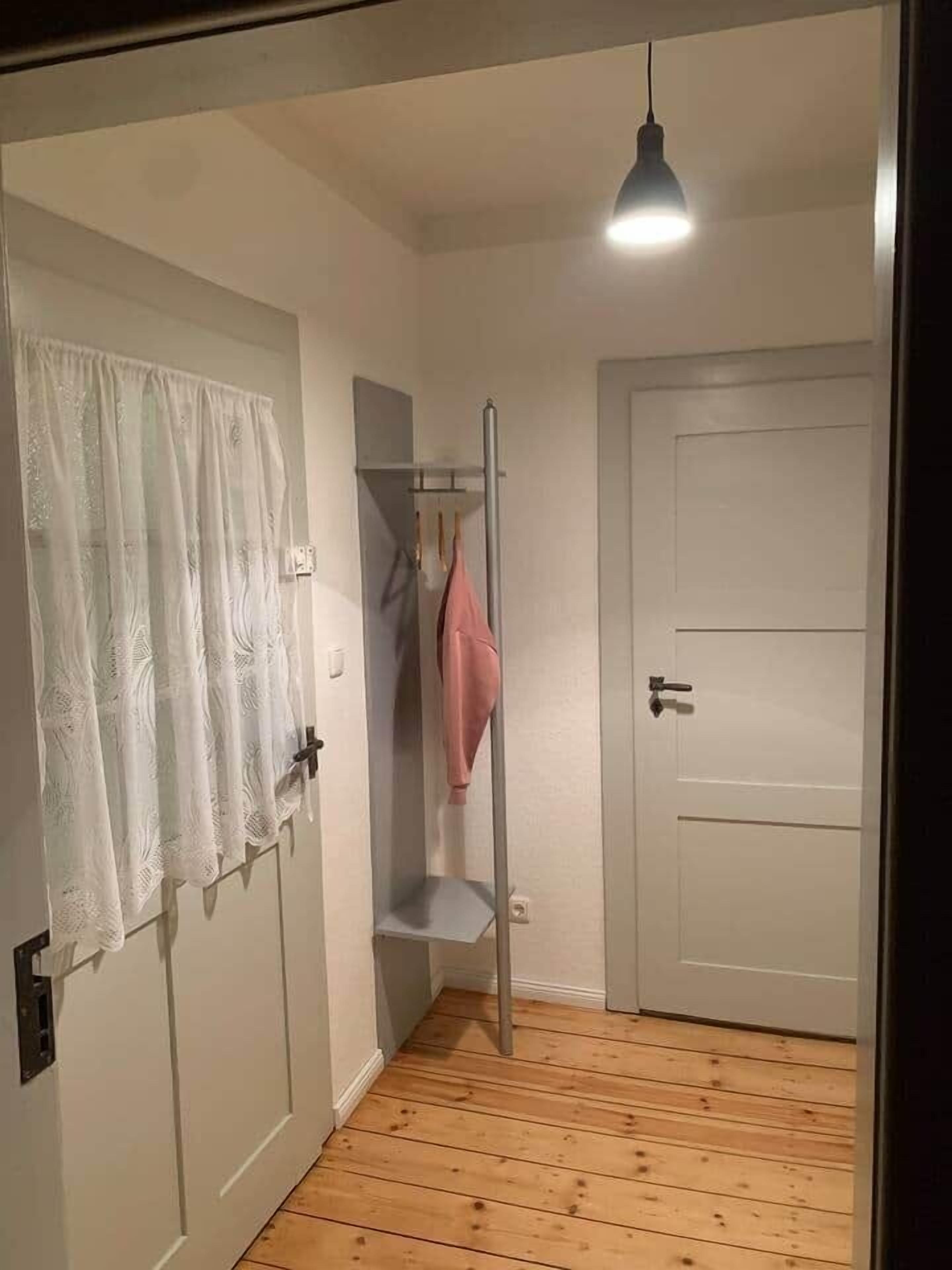 A room with a wooden floor, a white door, a closet with a hanging rod, and a pendant light.
