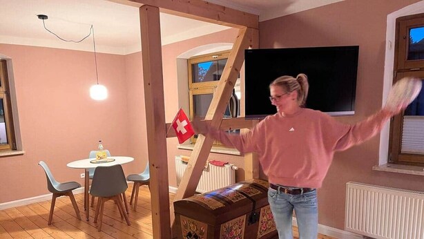 Een kamer met houten vloer, een eettafel met stoelen, een televisie en een Zwitserse vlag.