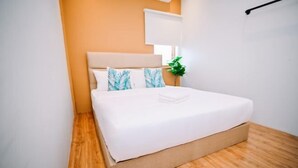 A neatly made bed with white bedding and blue leaf-patterned pillows in a room with wooden flooring and a beige headboard. - Swing & Pillows @ Armenian Victoria , Georgetown Penang (George Town)