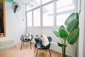 A room with a large window, two chairs, a small table with a plant, and a wall-mounted fan. - Swing & Pillows @ Armenian Victoria , Georgetown Penang (George Town)