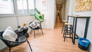 A modern interior with a wooden floor, a black chair with a cushion, a small table with a plant, and a wall with a corkboard. - Swing & Pillows @ Armenian Victoria , Georgetown Penang (George Town)