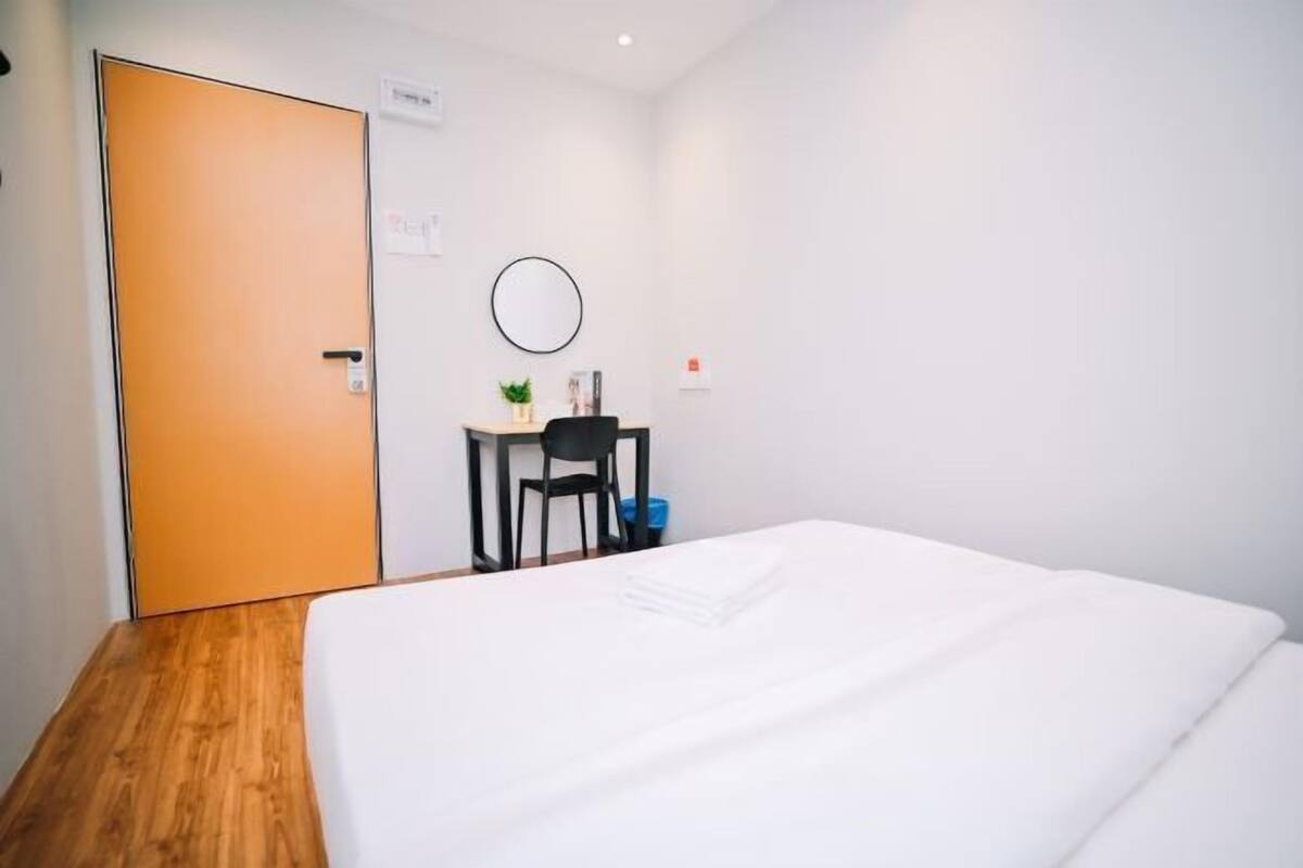 Hotellihuone, jossa on sänky, työpöytä, tuoli, pieni pöytä, jossa on kasvi, ja ovi.