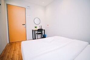Una camera d'albergo con un letto, una scrivania, una sedia, un piccolo tavolo con una pianta e una porta.