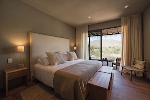 Un dormitorio con una cama grande, mesitas de noche, un banco, una silla y vistas al exterior.