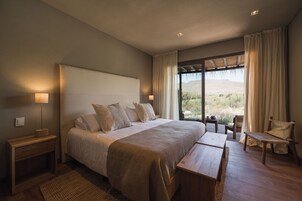 A bedroom with a large bed, bedside tables, a bench, a chair, and a view of the outdoors.