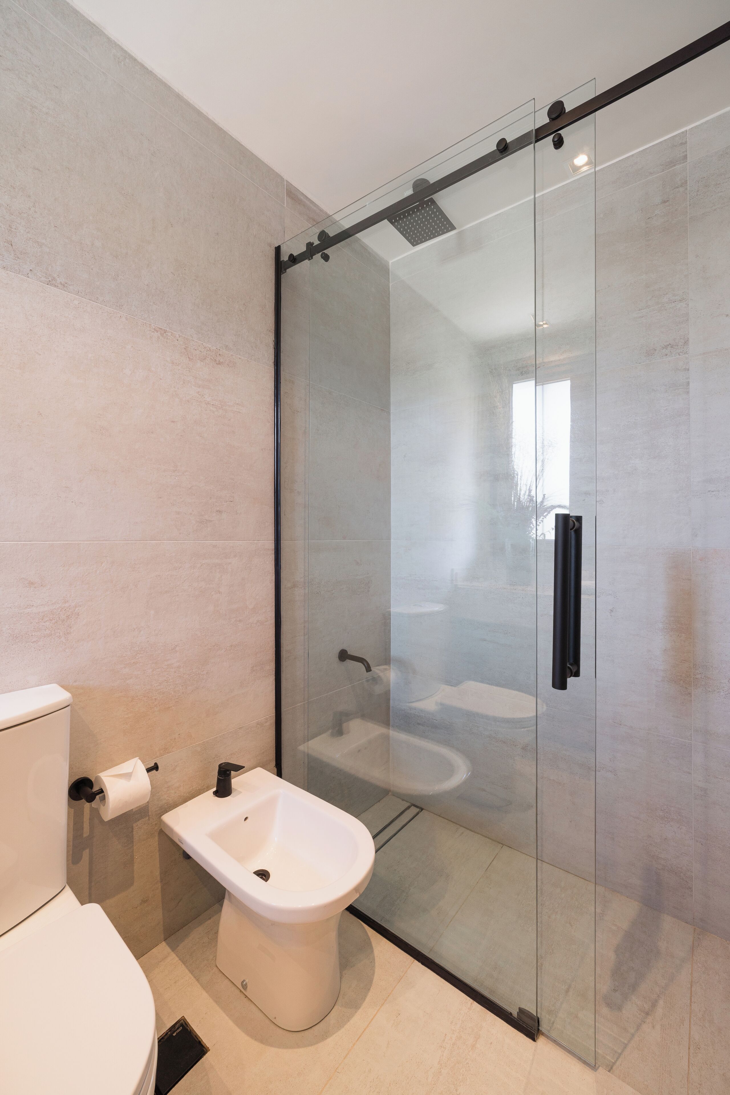 Et moderne badeværelse med en glasbrusekabine, et bidet og et toilet.