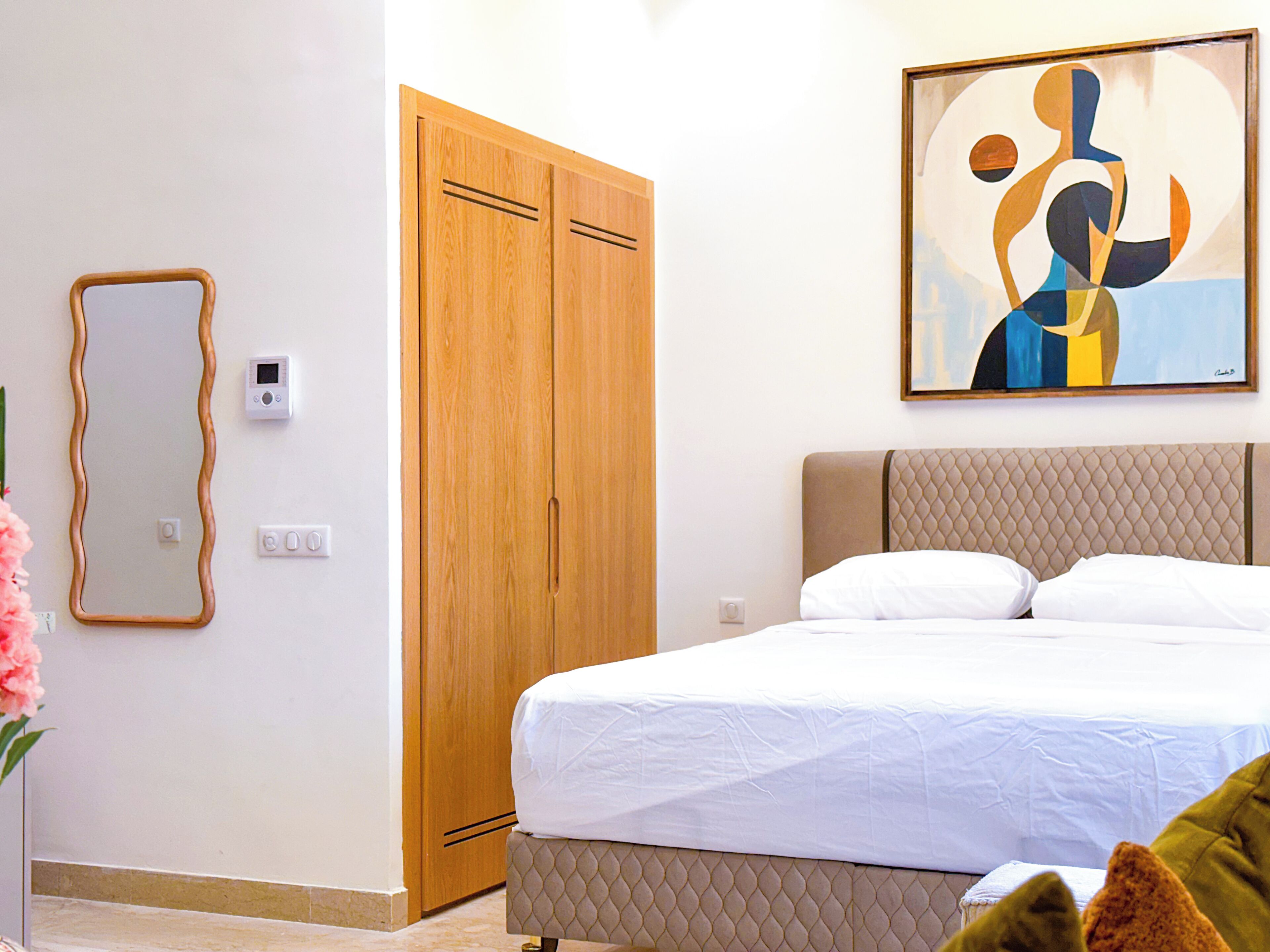Een slaapkamer met een bed, een houten garderobe, een spiegel en een schilderij aan de muur.
