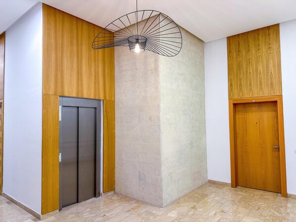 A modern interior with a wooden panel wall, a central light fixture, an elevator, and a wooden door. - Cozy Luxurious Bourgogne Studio (Casablanca)
