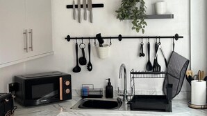 A modern kitchen with a black clock, knife rack, hanging utensils, a sink, and a washing machine. - Station View | Family | Parking | WIFI | Sleeps 6 (Leicestershire)