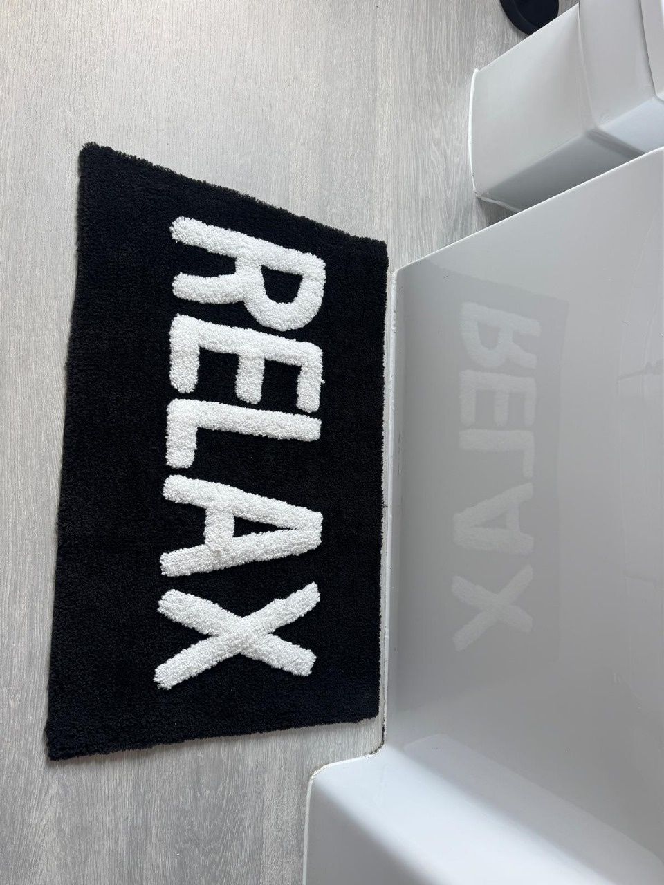 Une serviette noire et blanche avec le mot « RELAX » écrit dessus, le tout sur un mur blanc.