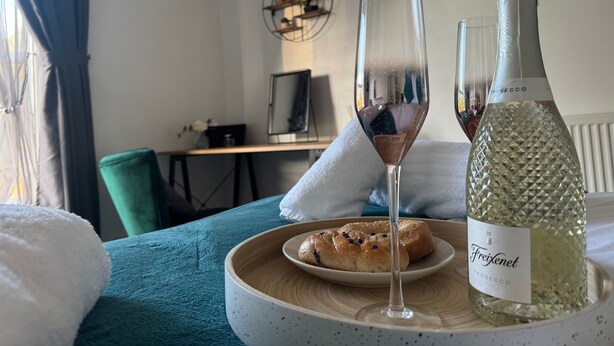 A room with a bed, a bottle of Freixenet Prosecco, two glasses, and a plate of pastries. - Station View | Family | Parking | WIFI | Sleeps 6 (Leicestershire)