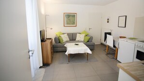 A compact living space with a sofa, a small table, a television, and a kitchenette. - "im Schiller" - Holiday Apartment in the Vineyards (Wiesenbronn)
