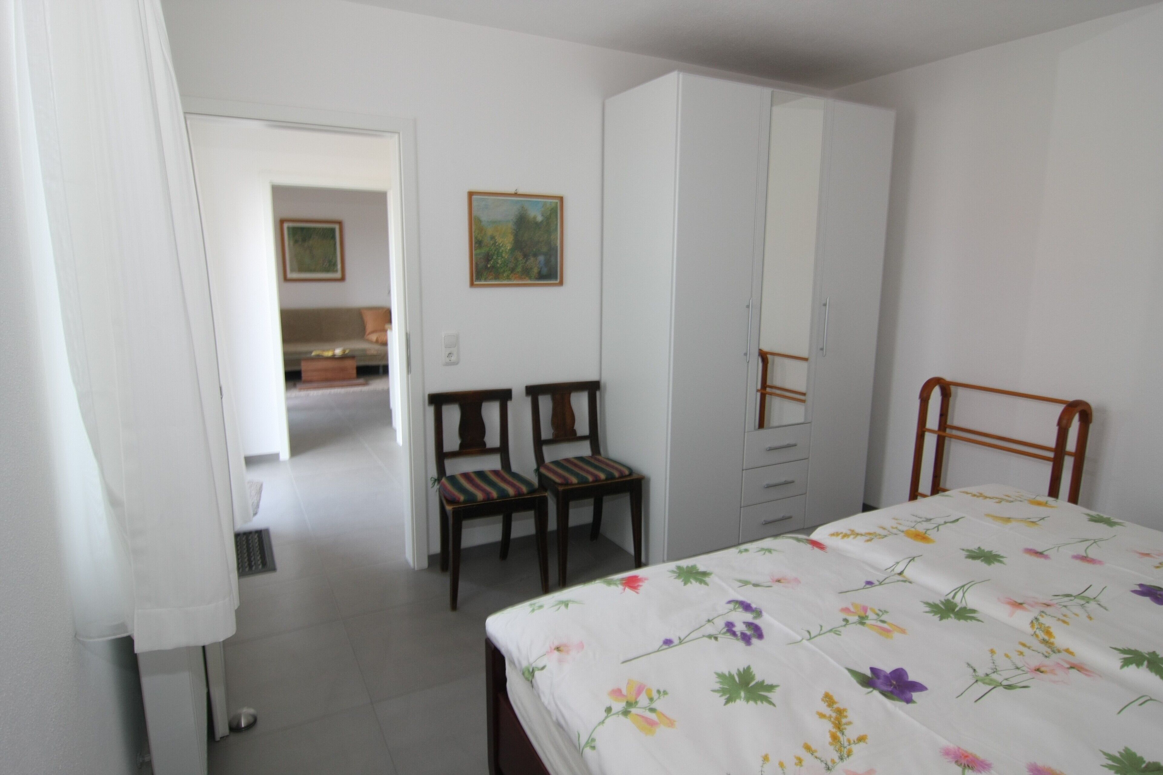 Een slaapkamer met een bed, een kledingkast, een bureau met stoel en een schilderij aan de muur.