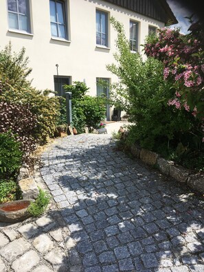 Un chemin pavé de pierres menant à un bâtiment doté de nombreuses fenêtres et d’une porte.