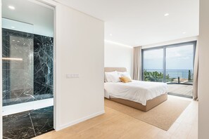 A modern bedroom with a large bed, a view of the ocean, and a balcony.