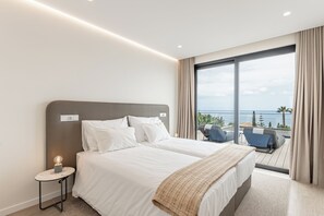 A hotel room with two beds, a nightstand, and a balcony with a view of the sea. - Eco Fajã Villas - Deluxe - A sanctuary 60m above sea level (Arco da Calheta)