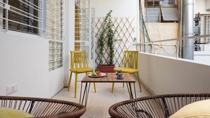 A balcony with yellow chairs, a table with a plate of fruit, and a potted plant. - Boho-Chic Cozy 2BR - Apt & Balcony in Mar Mikhael (Beirut)
