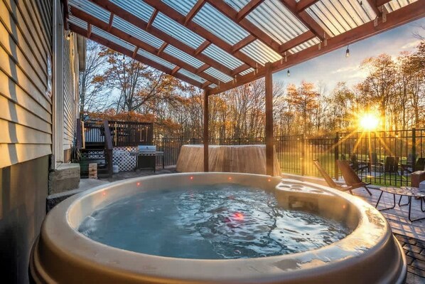 Uma banheira de hidromassagem sob uma pérgola, com vista para árvores e um pôr do sol.