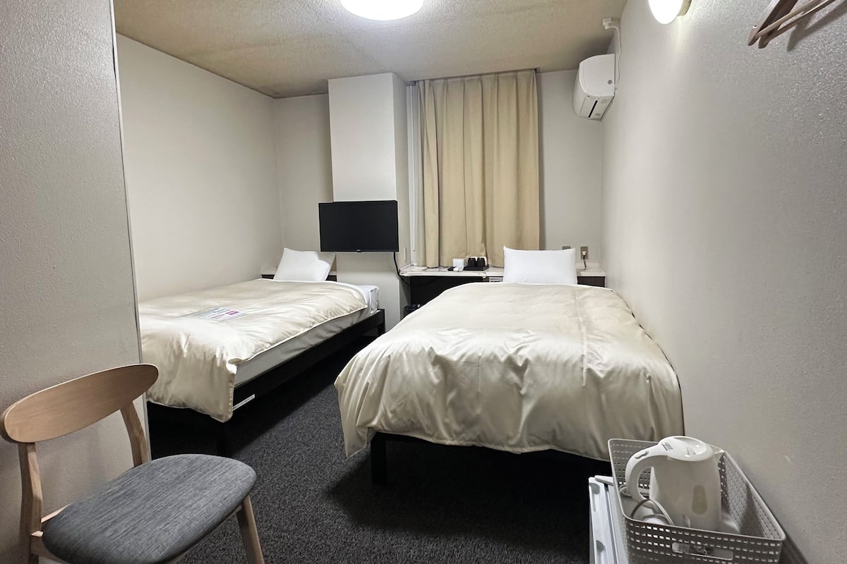 Habitación de hotel con dos camas, un escritorio, una silla, una lámpara, un televisor y un ventilador de techo.