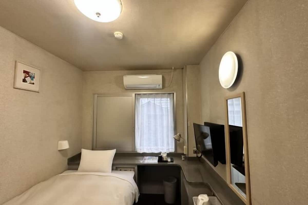 Una habitación de hotel con cama, escritorio, silla, televisor y aire acondicionado.