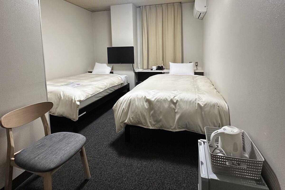 Habitación de hotel con dos camas, un escritorio, una silla, una lámpara de escritorio, aire acondicionado de pared y un cubo de basura.