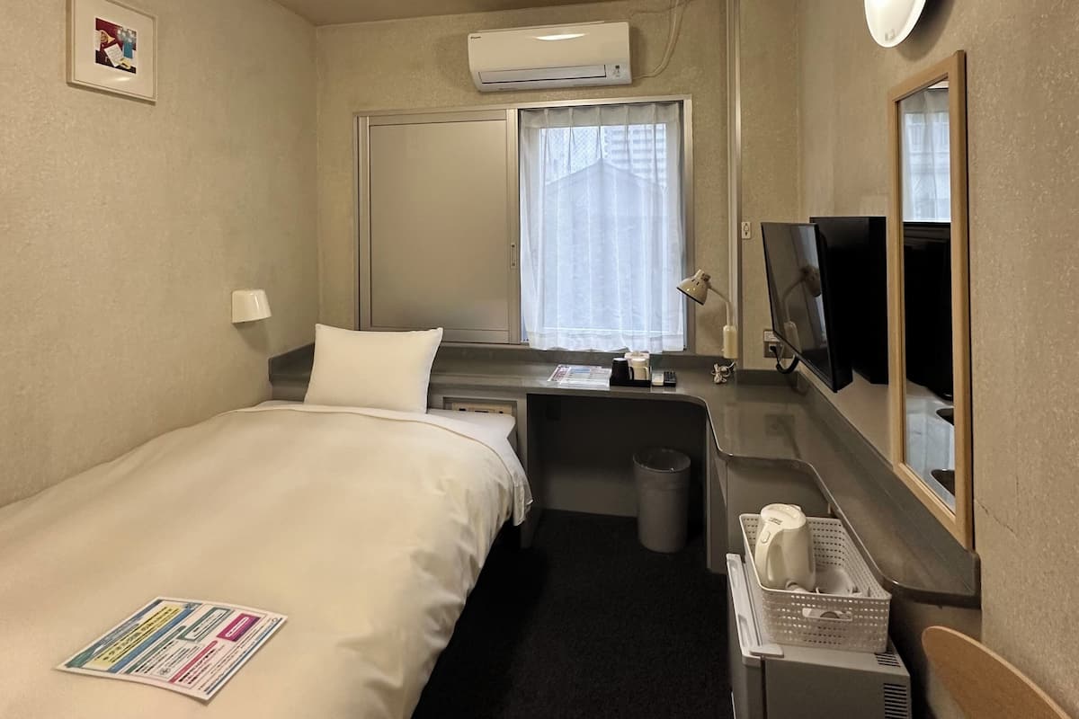 Una habitación de hotel con cama, escritorio, silla, televisión y aire acondicionado.