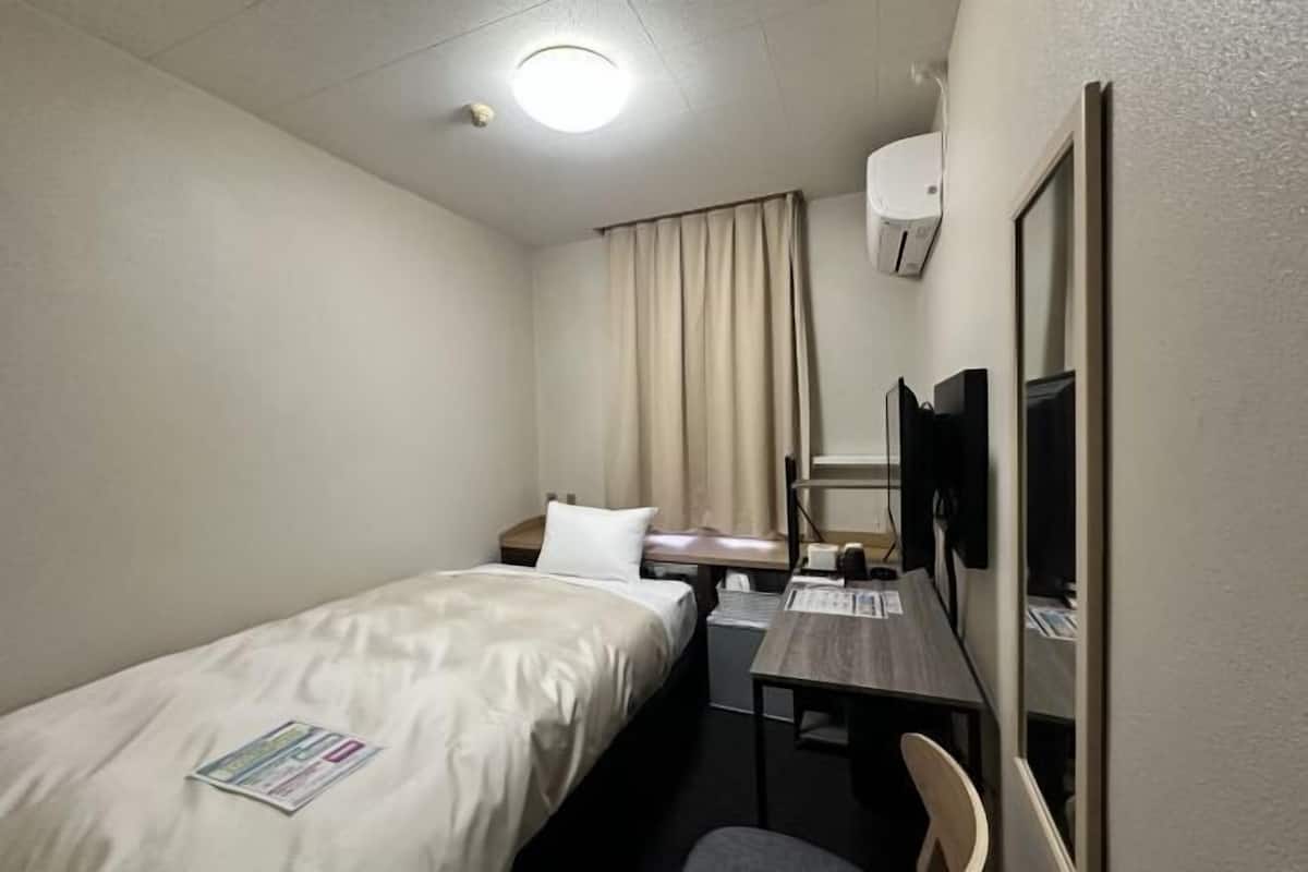 Habitación de hotel con cama, escritorio, silla, televisor y unidad de aire acondicionado.