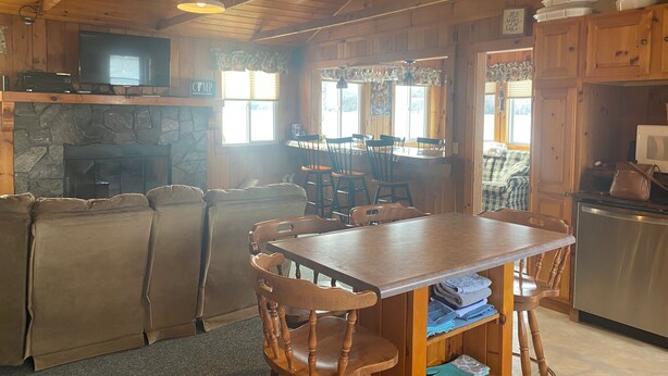 A cozy cabin-style interior with a stone fireplace, wooden dining table, and chairs. - 3 Bedroom Lakefront home on Maidstone Lake (Maidstone)