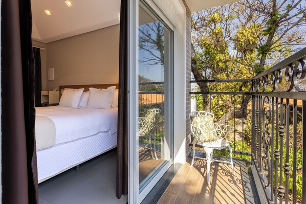 A bedroom with a bed, a balcony with a chair, and a view of trees. - Onze Tuin (Holambra)