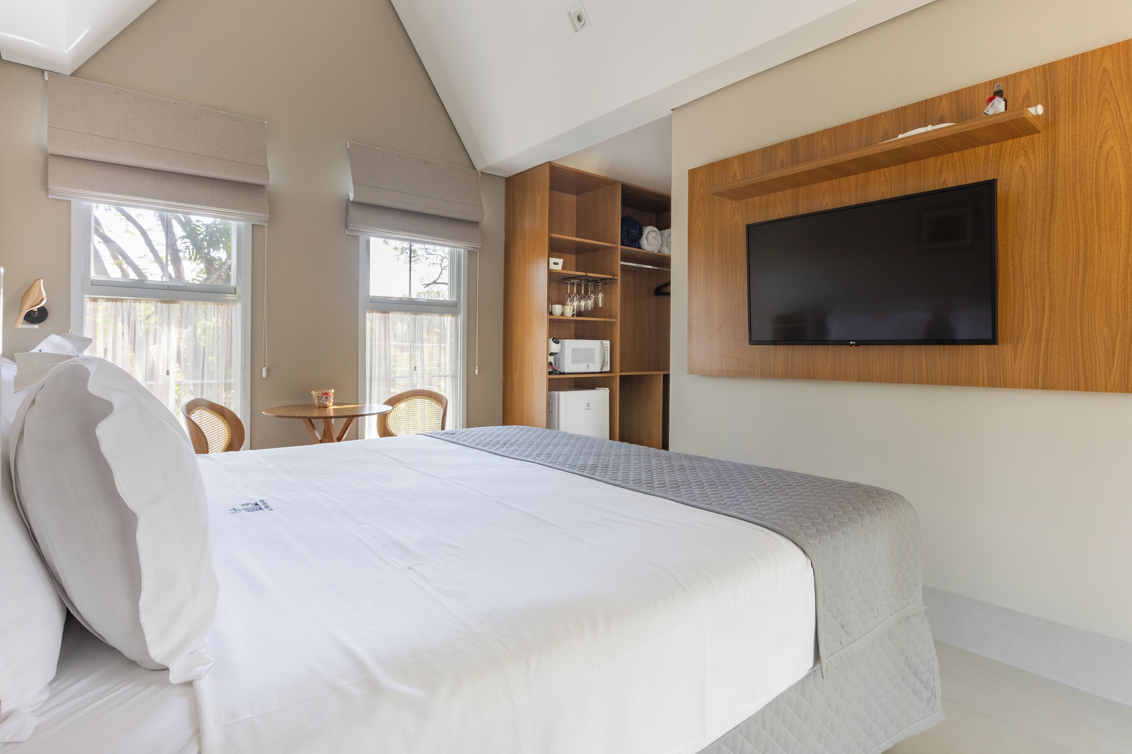Un dormitorio con una cama grande, televisión montada en la pared, una mesita pequeña y una silla.