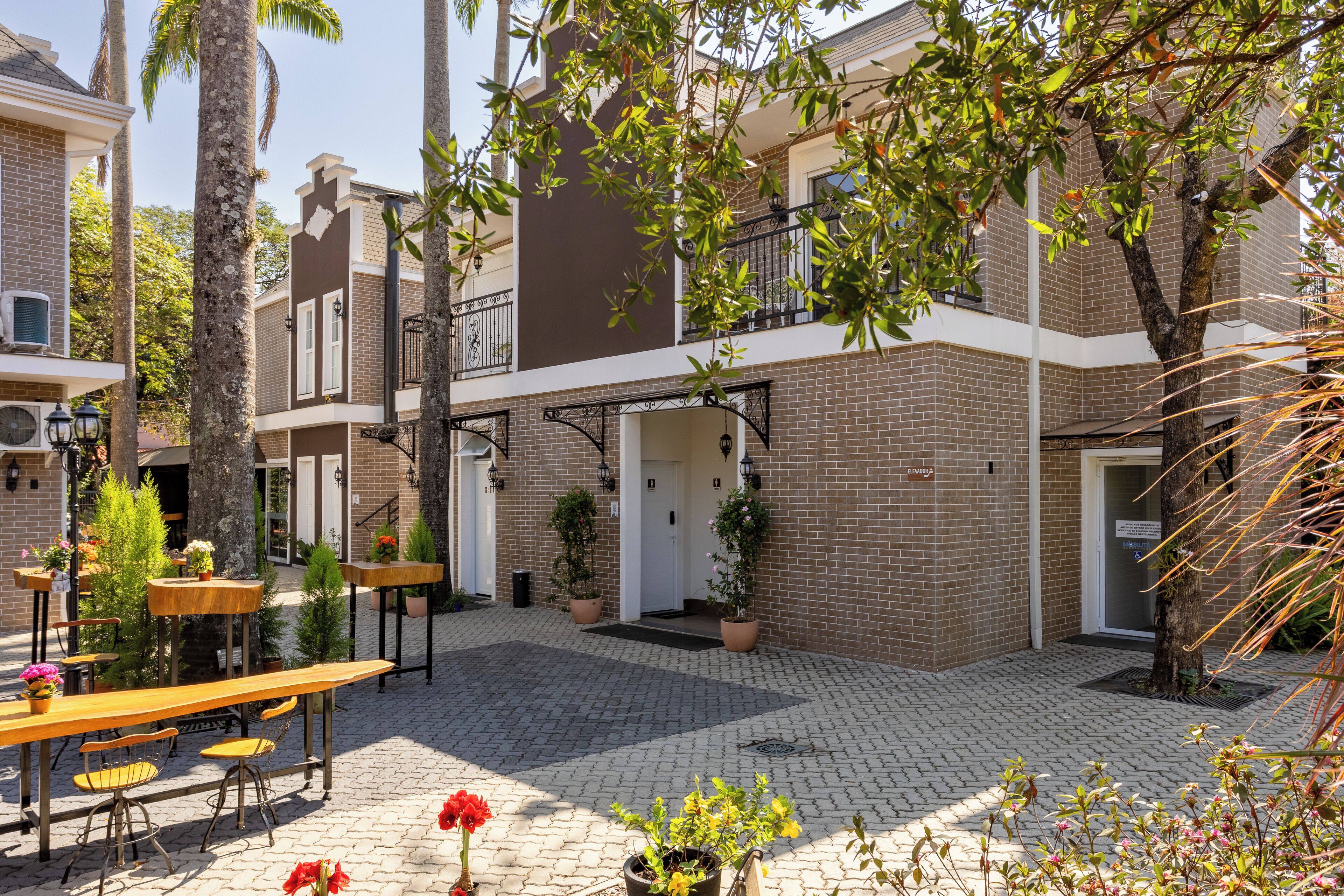 A courtyard with outdoor seating, potted plants, and a brick building with a balcony.
