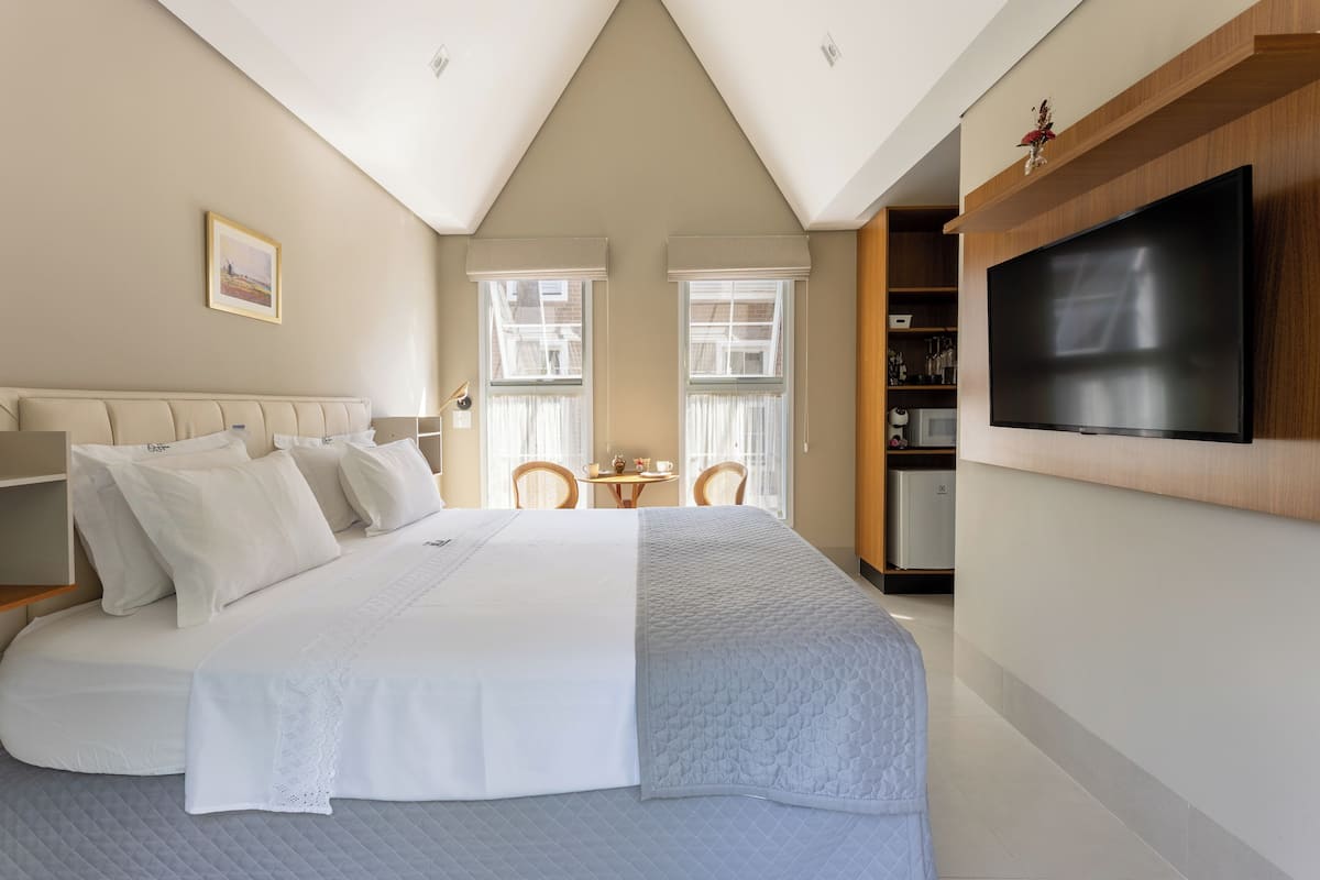 A bedroom with a large bed, a TV mounted on the wall, and a small table with chairs.