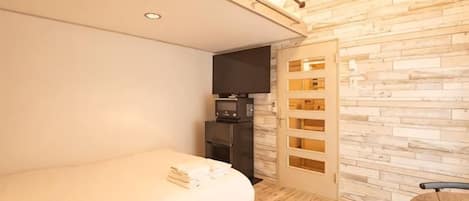 Habitación de hotel moderna con cama, televisor de pantalla plana, pared de madera y un escritorio pequeño.