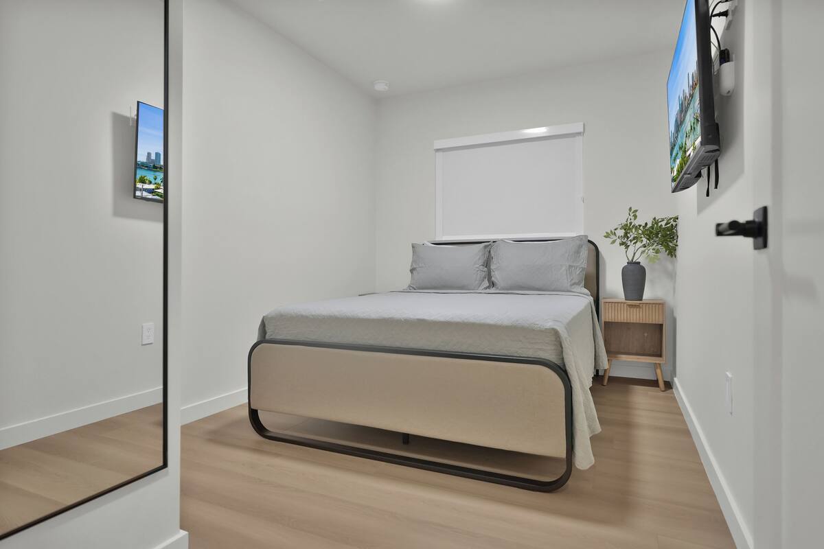 A modern bedroom with a bed, a TV mounted on the wall, and a small bedside table with a plant.