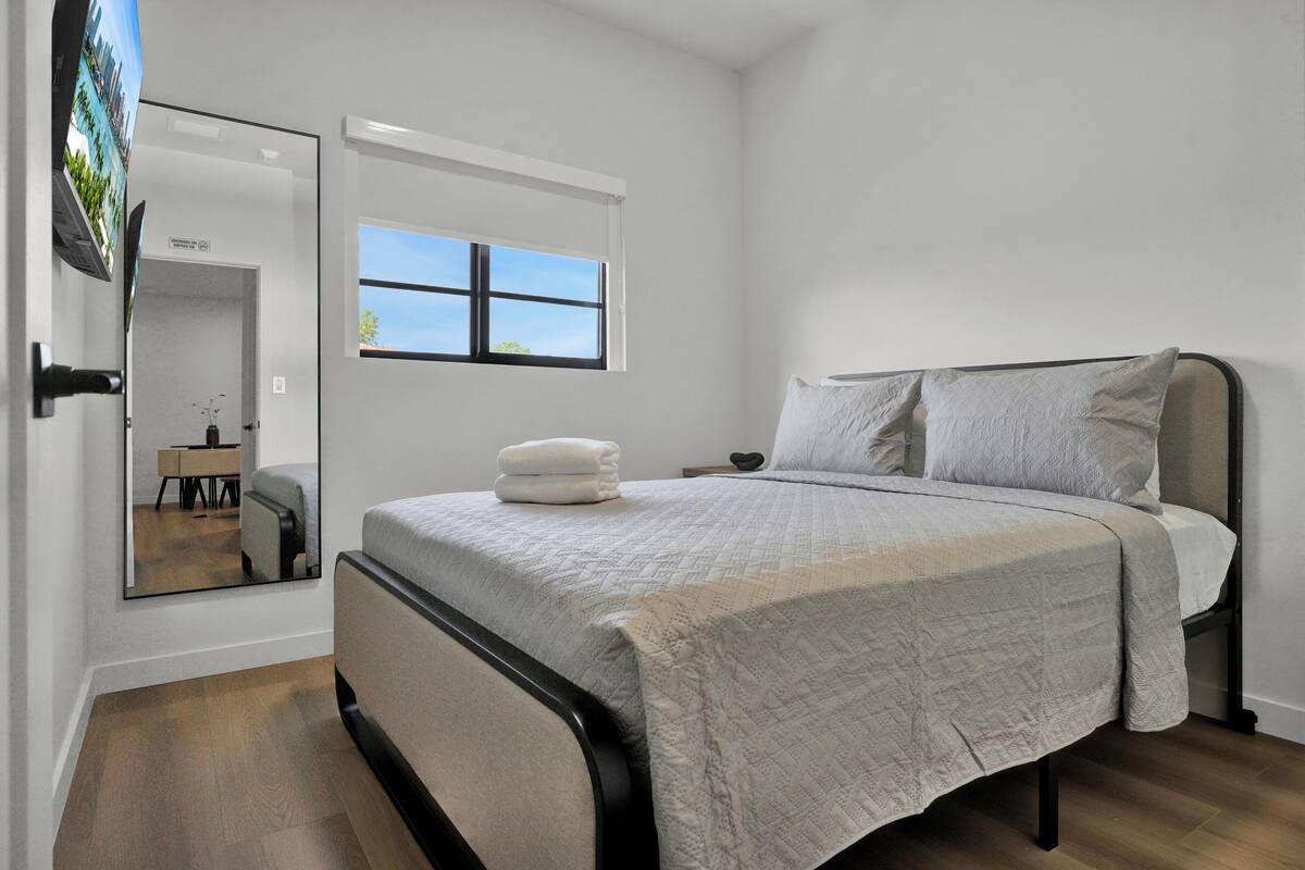 A bedroom with a bed, a window, a mirror, and a television.