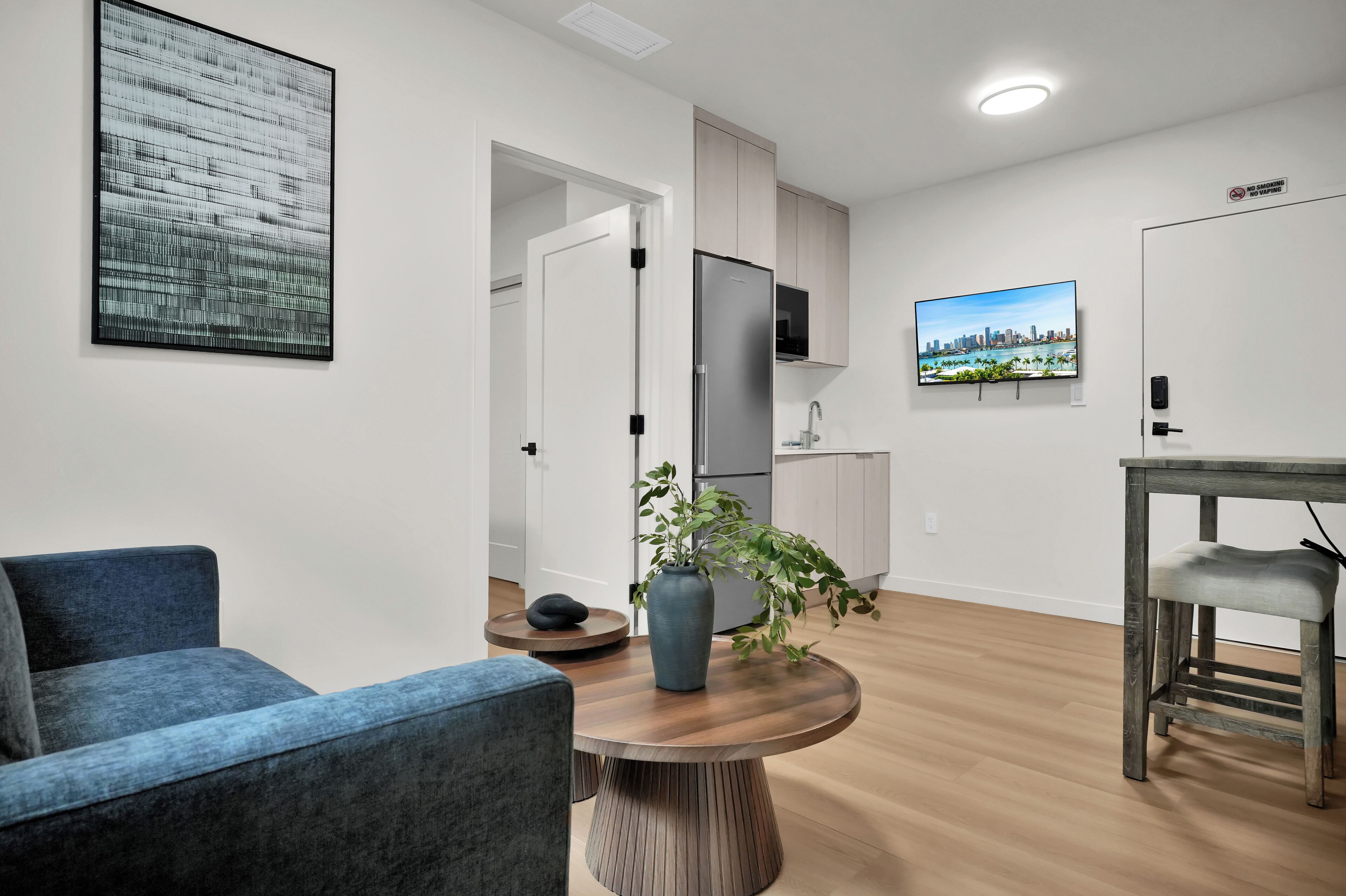 Un salon moderne avec une table basse ronde en bois, un canapé bleu, une plante en pot et un téléviseur fixé au mur.