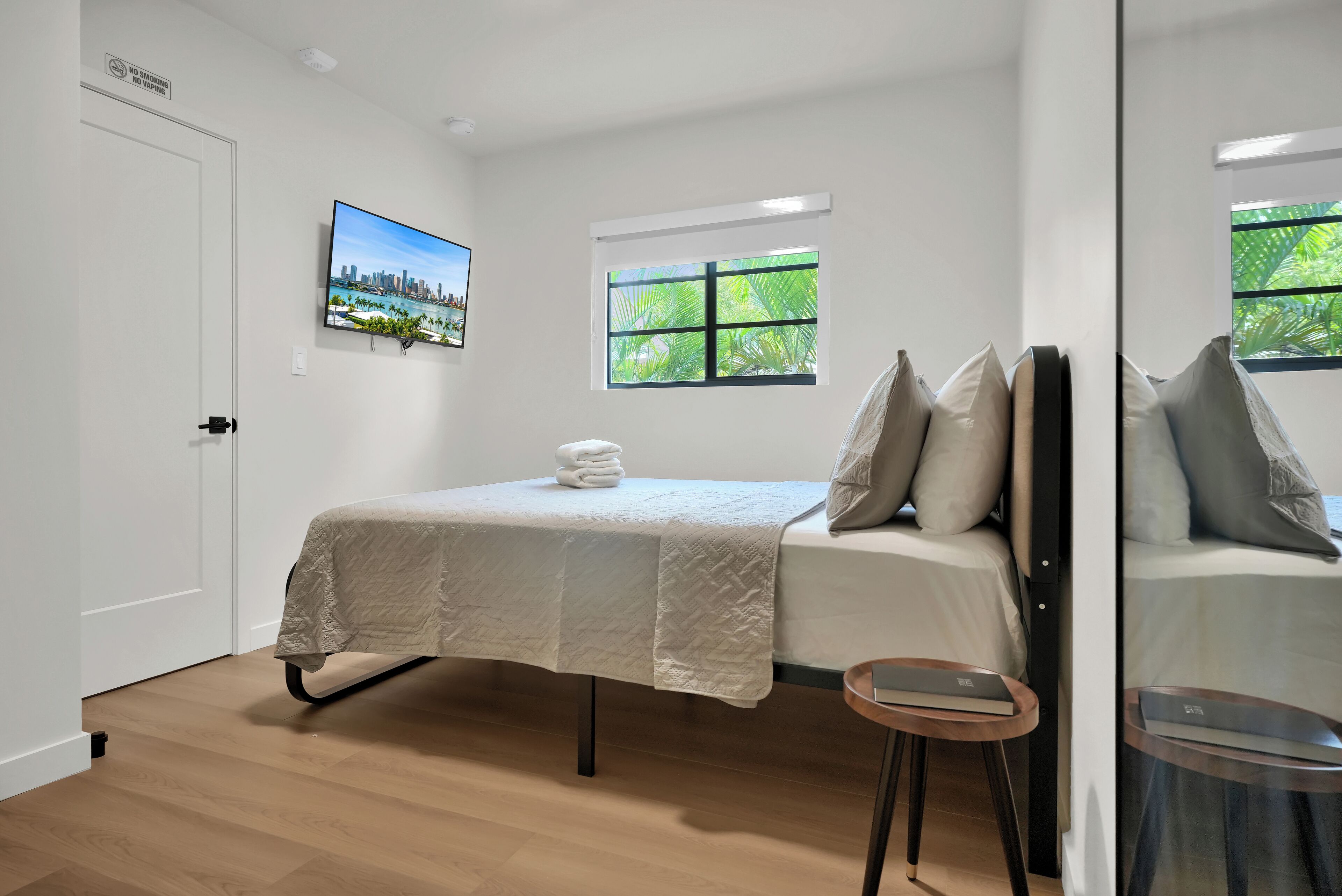 A hotel room with a bed, a small table, a TV, a window, and a door.