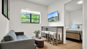 Un soggiorno moderno con un divano grigio, un tavolino da caffè in legno con una pianta e un quadro raffigurante una veduta cittadina sulla parete.